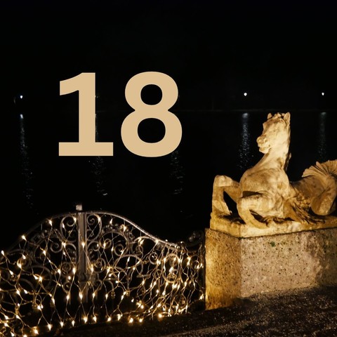 Photograph (colour): Stone horse in the dark as part of a porte that is illuminated with golden lights. In the middle the number 18.