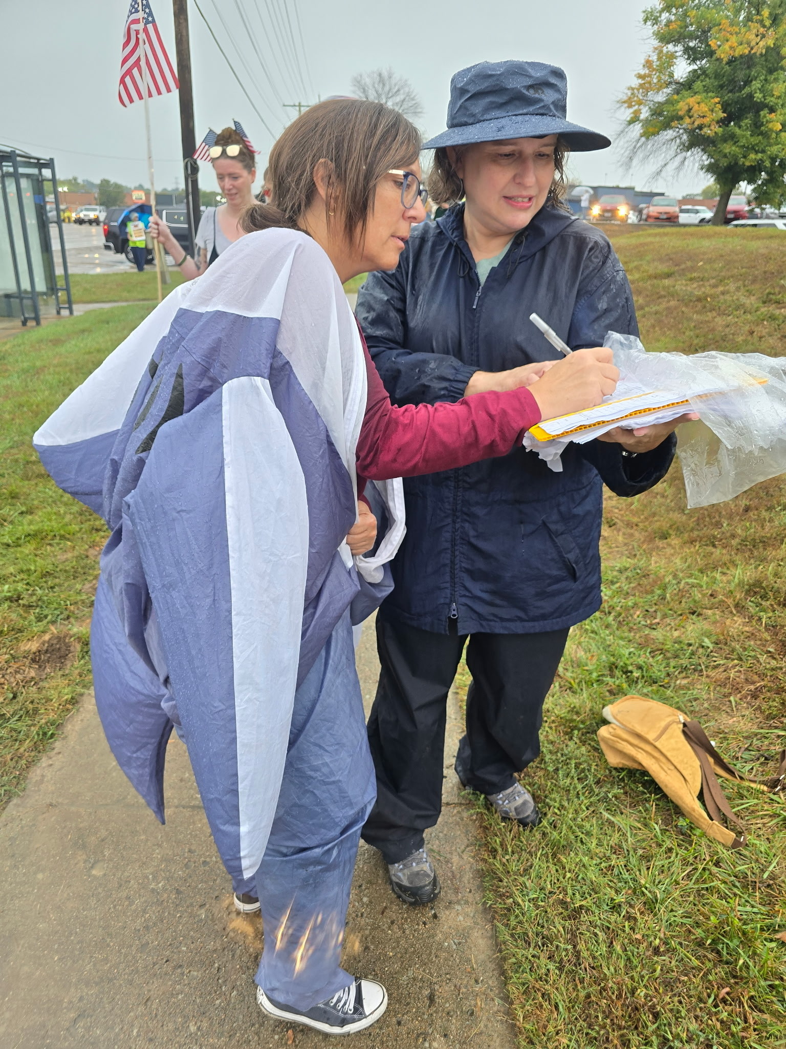 A person in an inflatable shark costume signs a petition held by a person in rain gear.