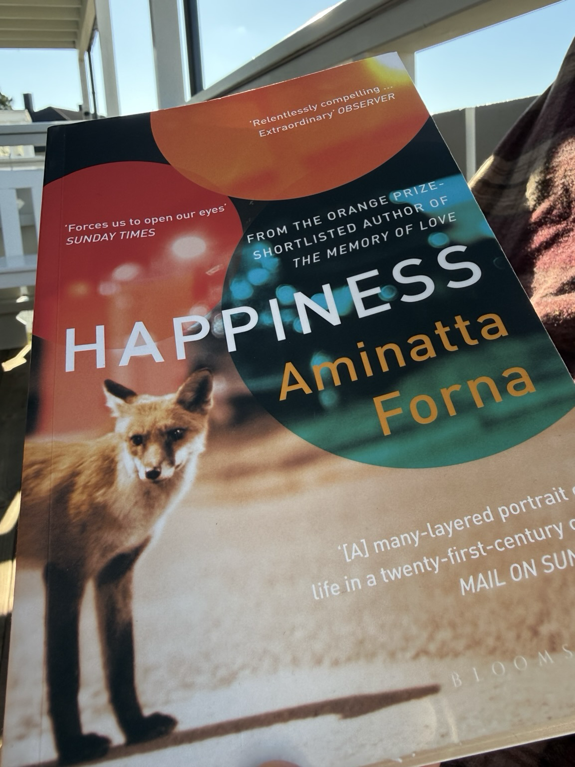 Cover of Happiness showing a fox standing on sepia geound while coloured blobs in red, orange, anf blue shading to green hovers over it/ encircles the title and author name.