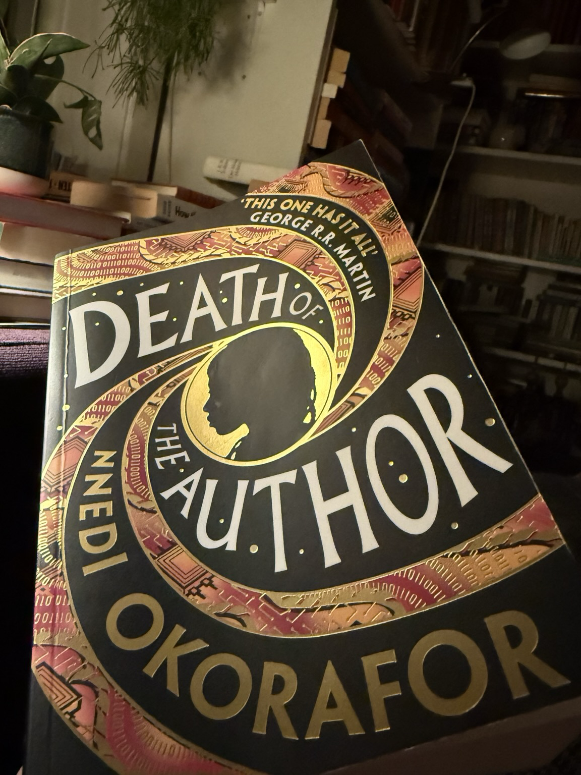 Cover of Death of the author. At the centre a black shadow profile. From this circle the title and the author name spiral outwards in alternating black and coloured lines. The coloured lines are computer-themed (1 and 0 strings and circuit boards), but recalling ankara patterns.