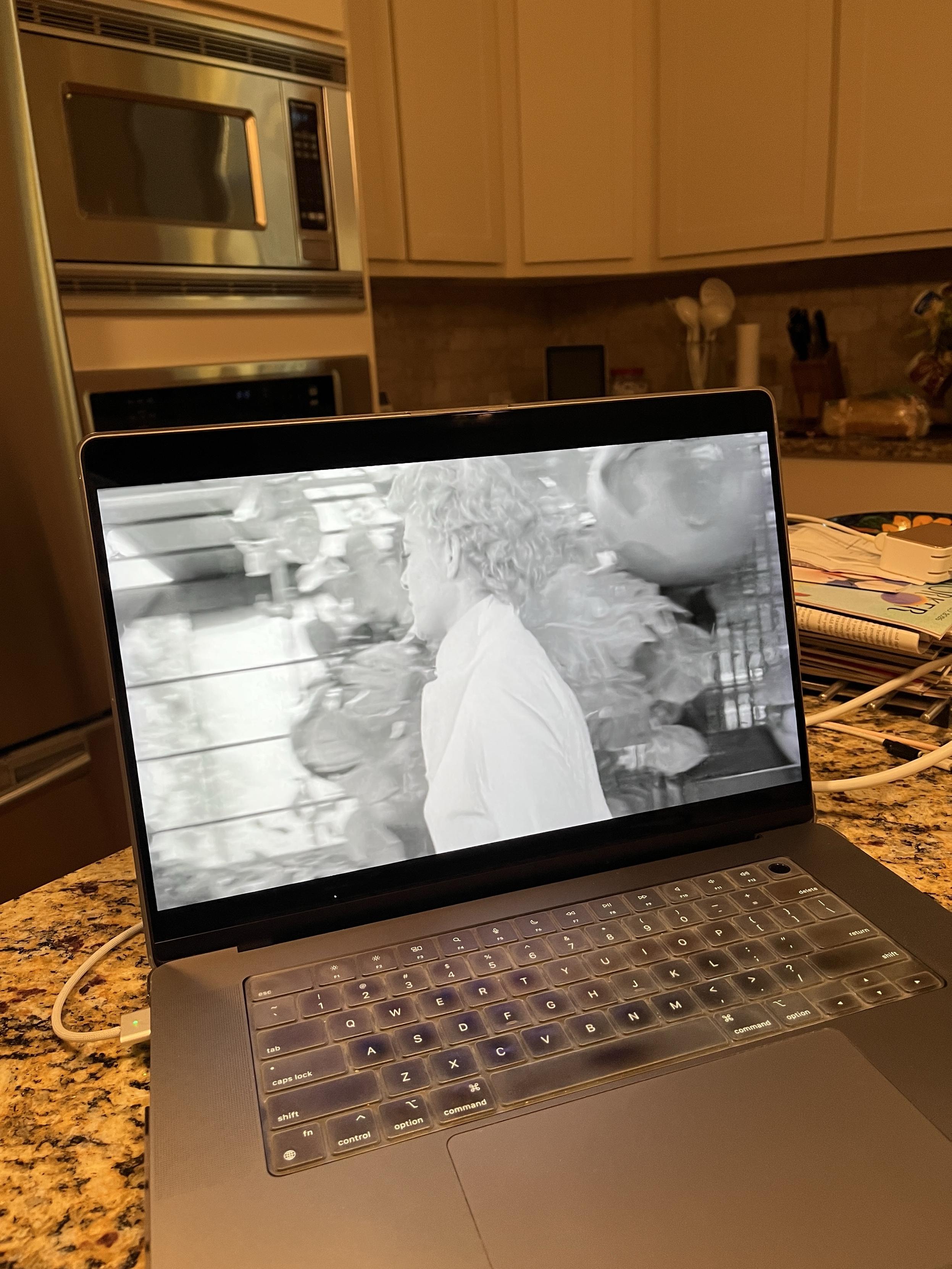Laptop showing a black and white shot of a woman walking in front of giant tomatoes