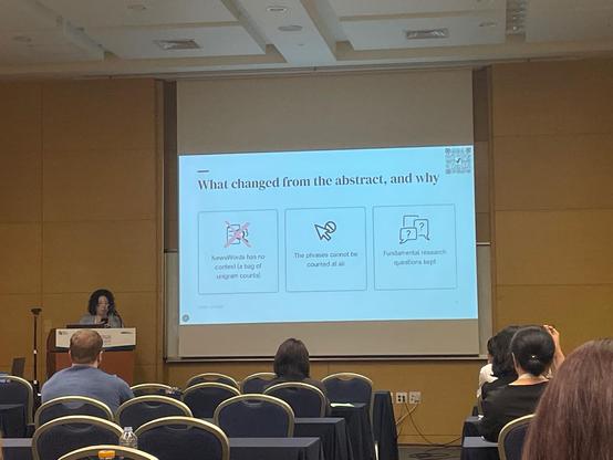 A slide on screen in a conference room. The heading says 'what changed from the abstract, and why'. The methods didn't work but the fundamental research questions were kept 