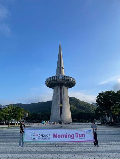 Blue sky, green mountain in the background, the Daejeon tower and a banner saying 'DH2026 morning run'