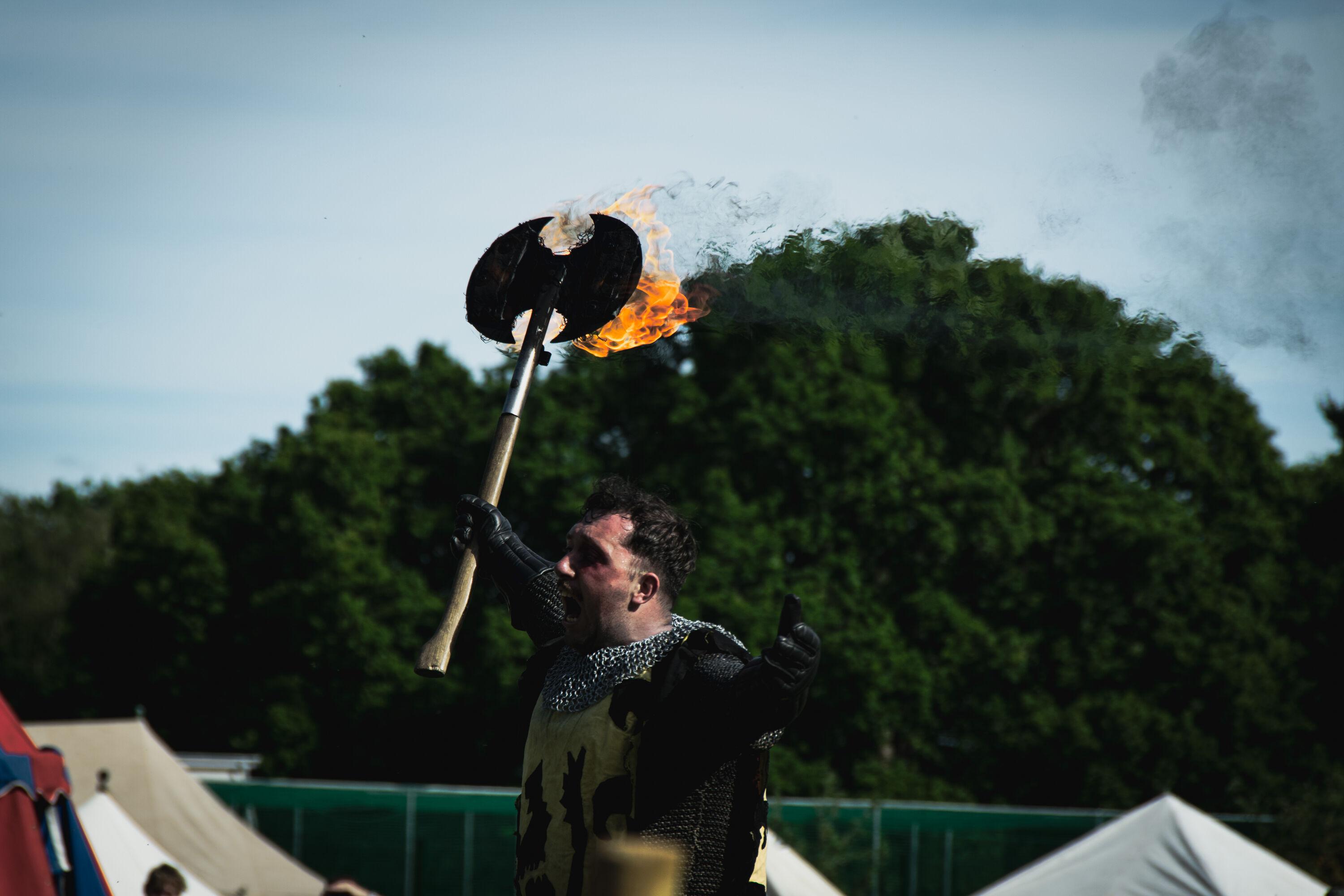 Male reenactor in medieval costume wielding a burning axe above his head.