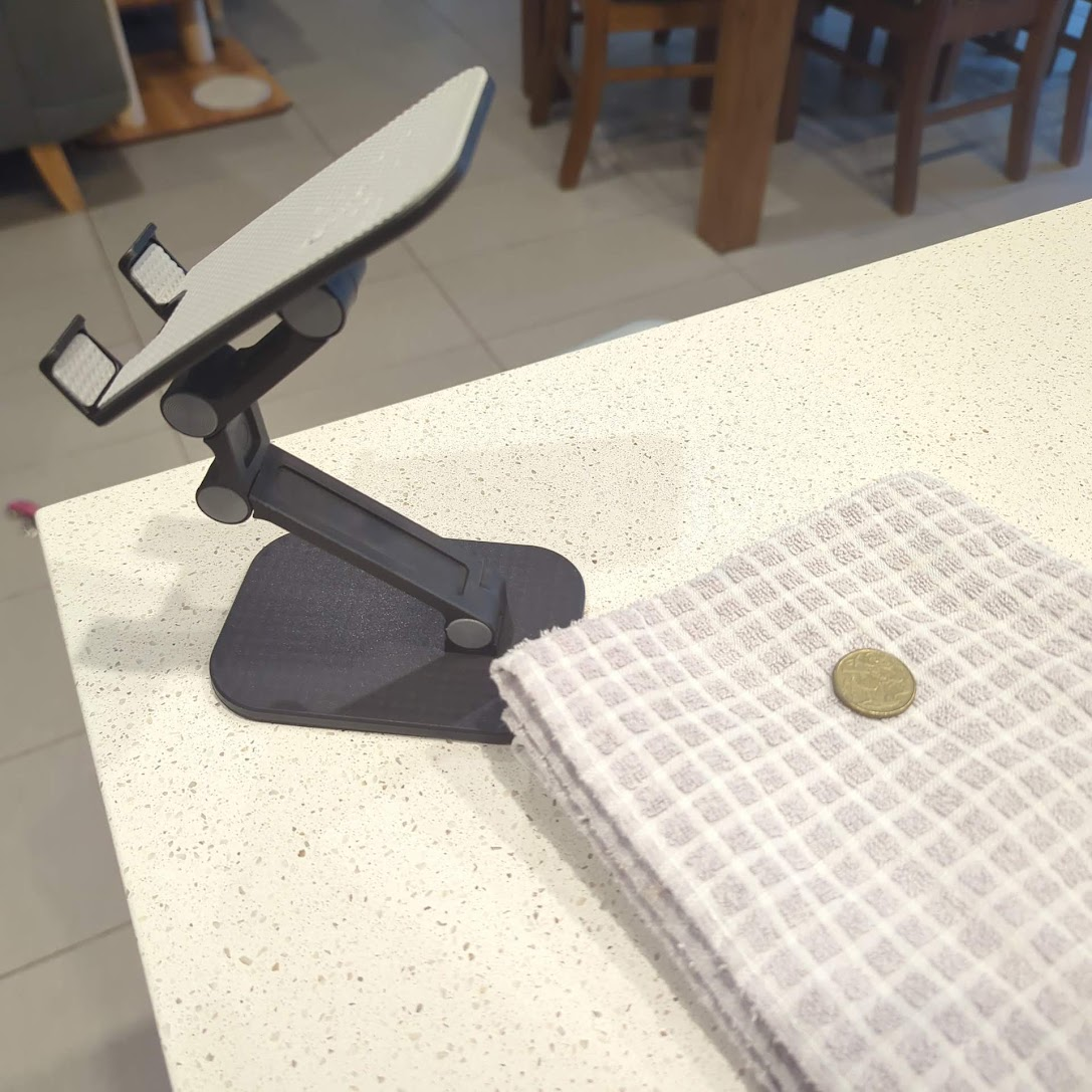 Foldable phone stand sitting next to a dollar coin on a tea towel on the bench