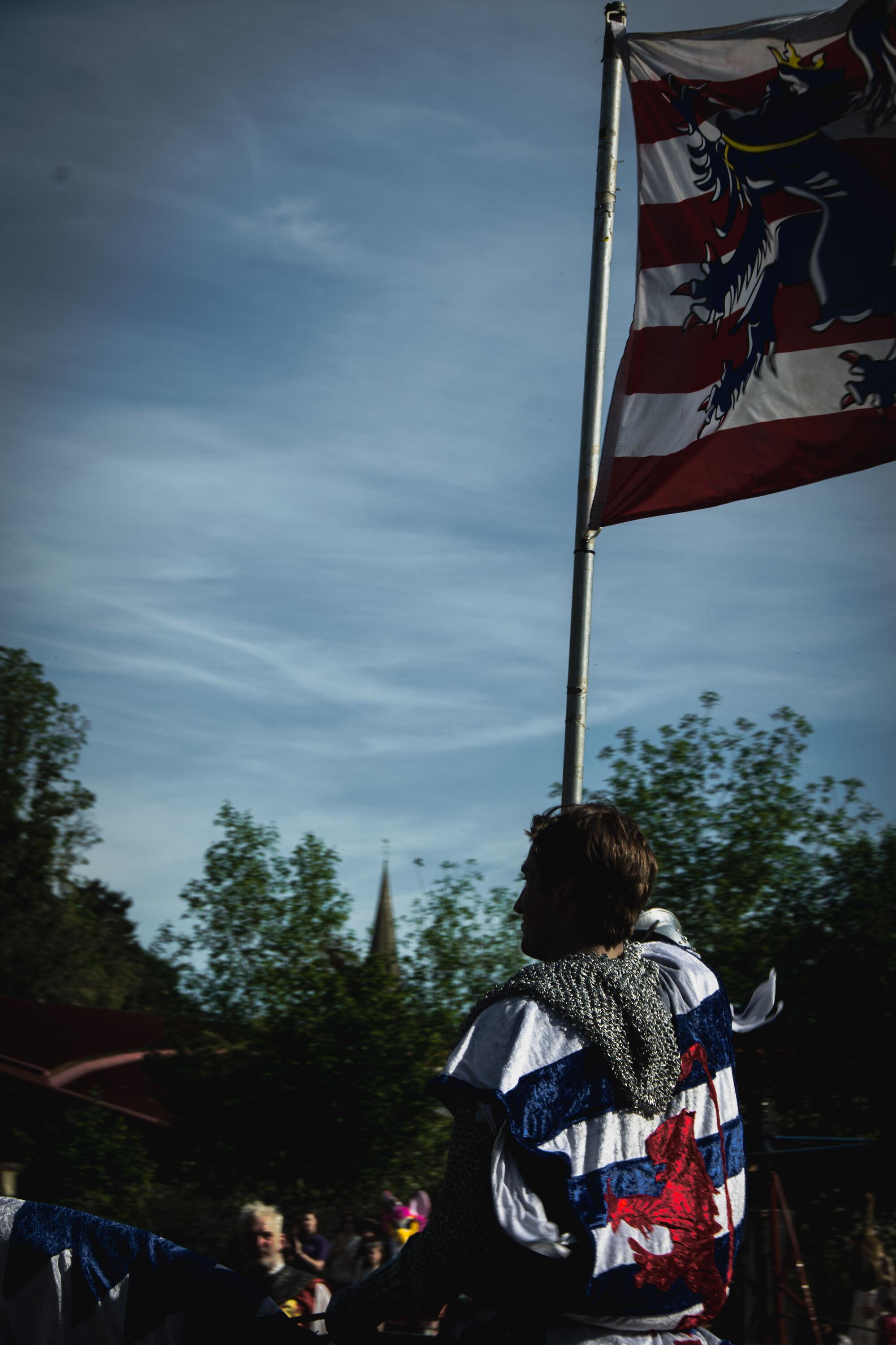 A reenactor dressed as a medieval knight carrying a flag.