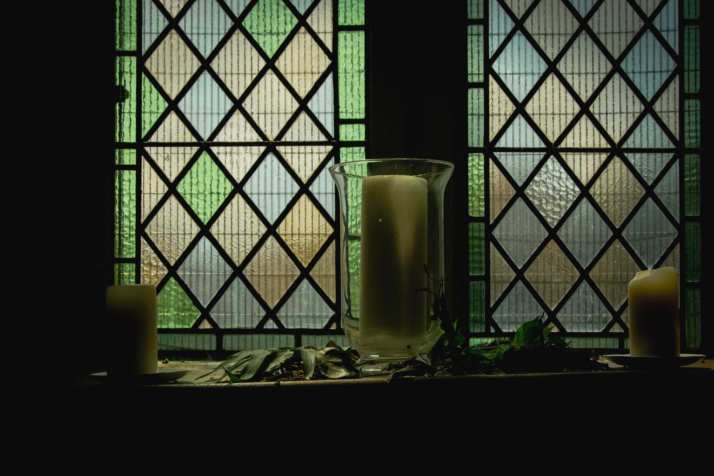 This is inside a church. Three candles in front of a coloured-glass window viewed from fairly close by.