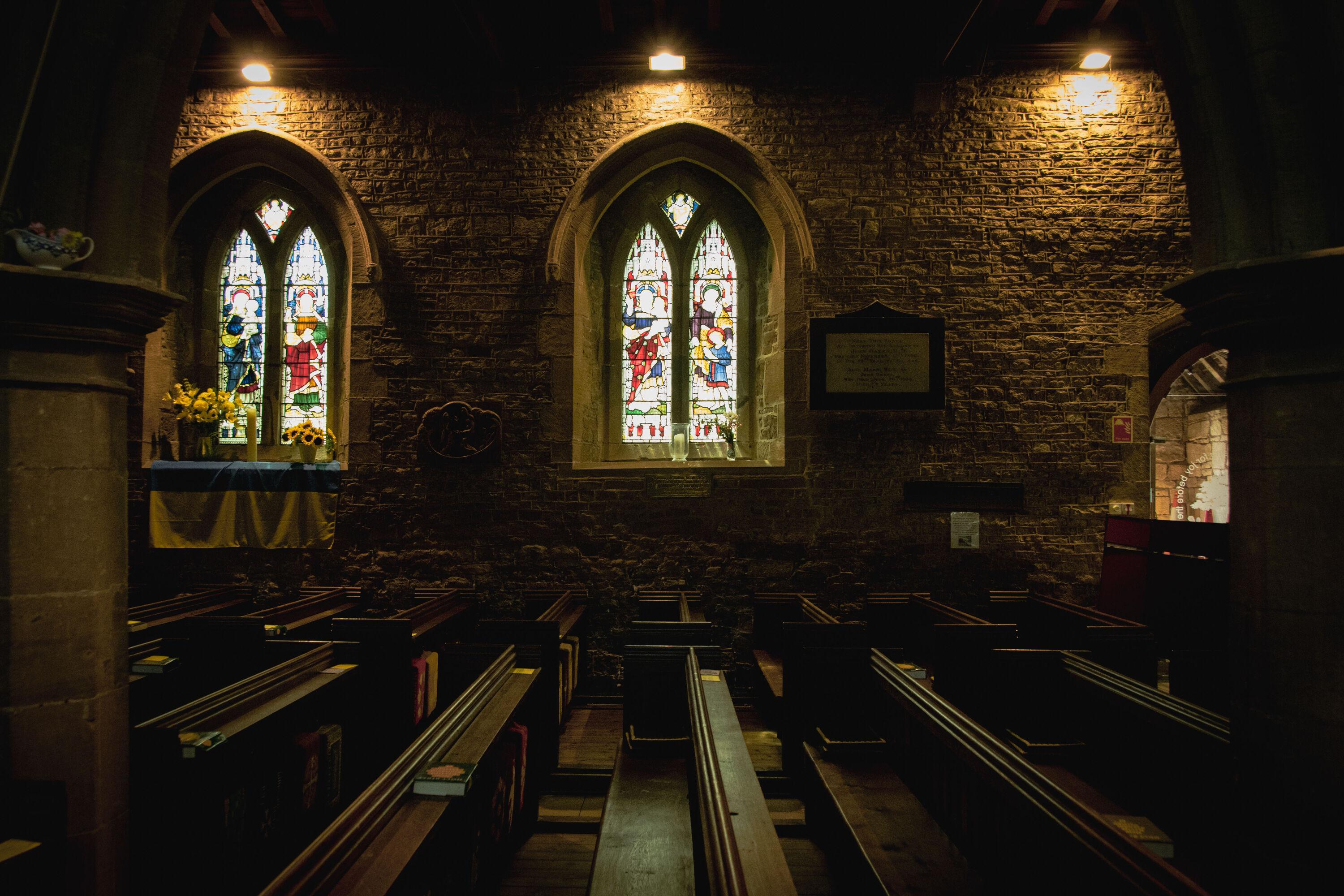Church interior: looking across the pews towards the south wall with two stained-glass windows.