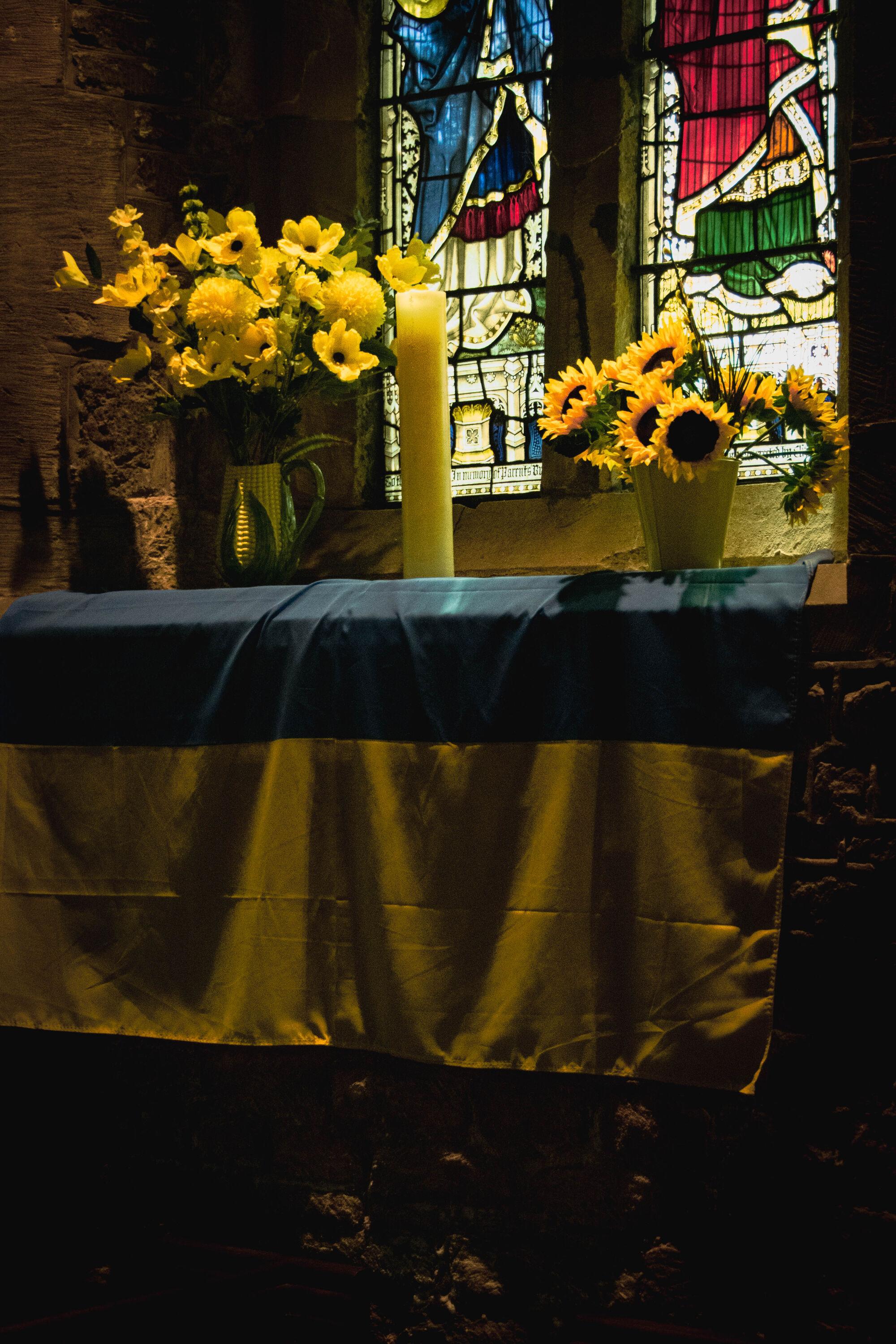 Church interior: a window sill with candle and flowers below a stained-glass window.