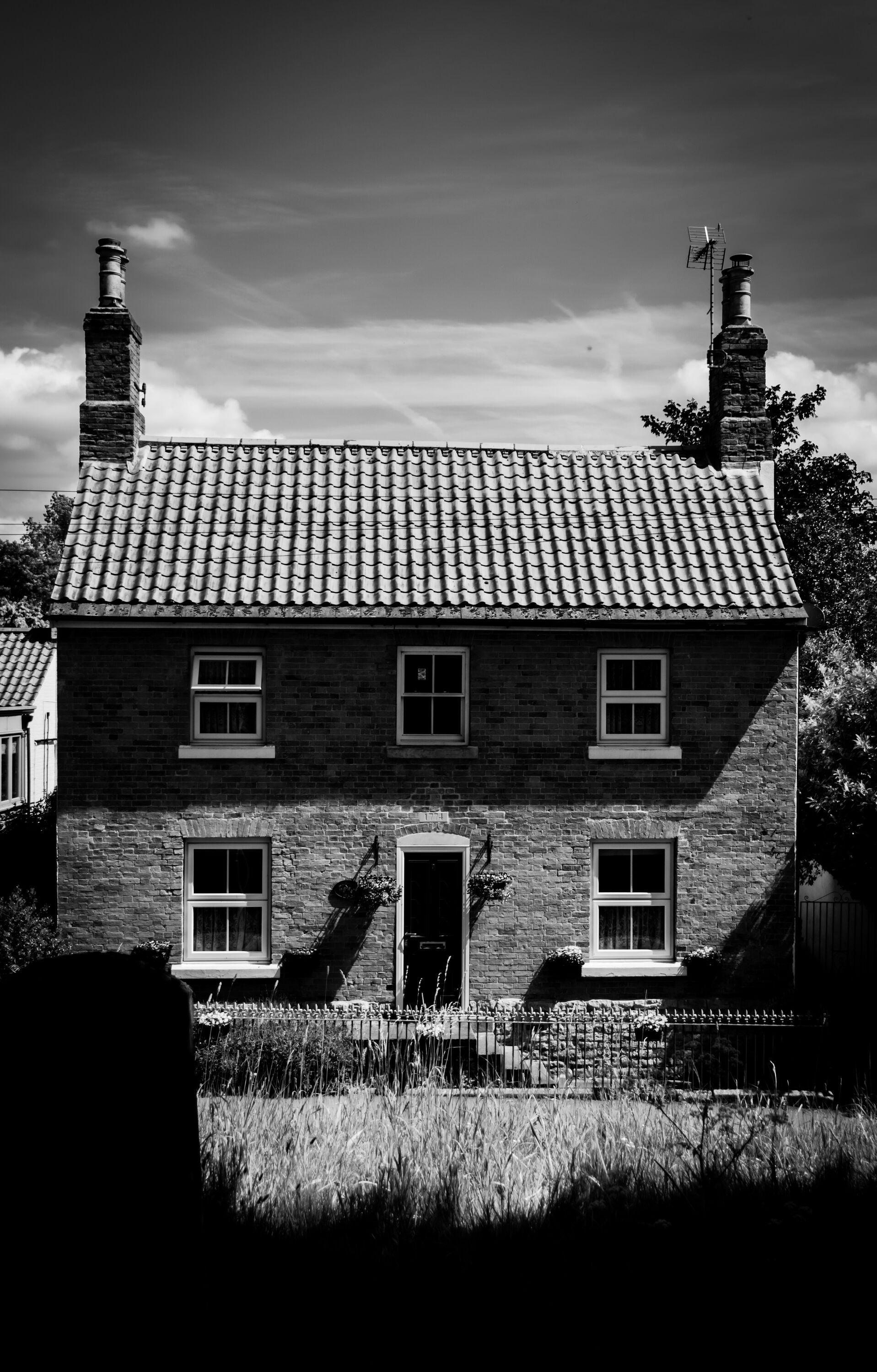 Black and white image of an old English house in the sunshine.