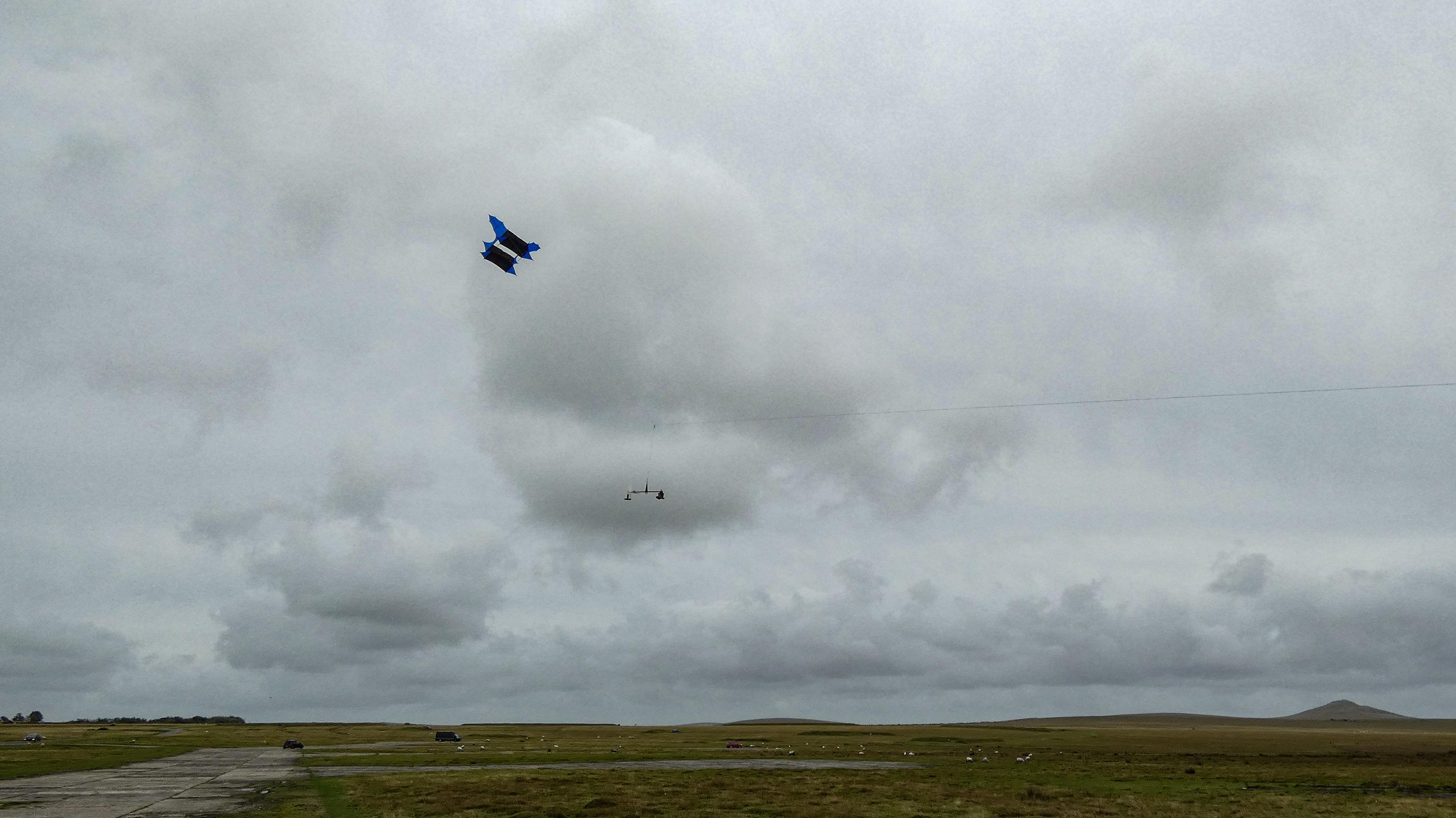A giant cody box kite rises into the air, with the kite drone sensor boom slung below