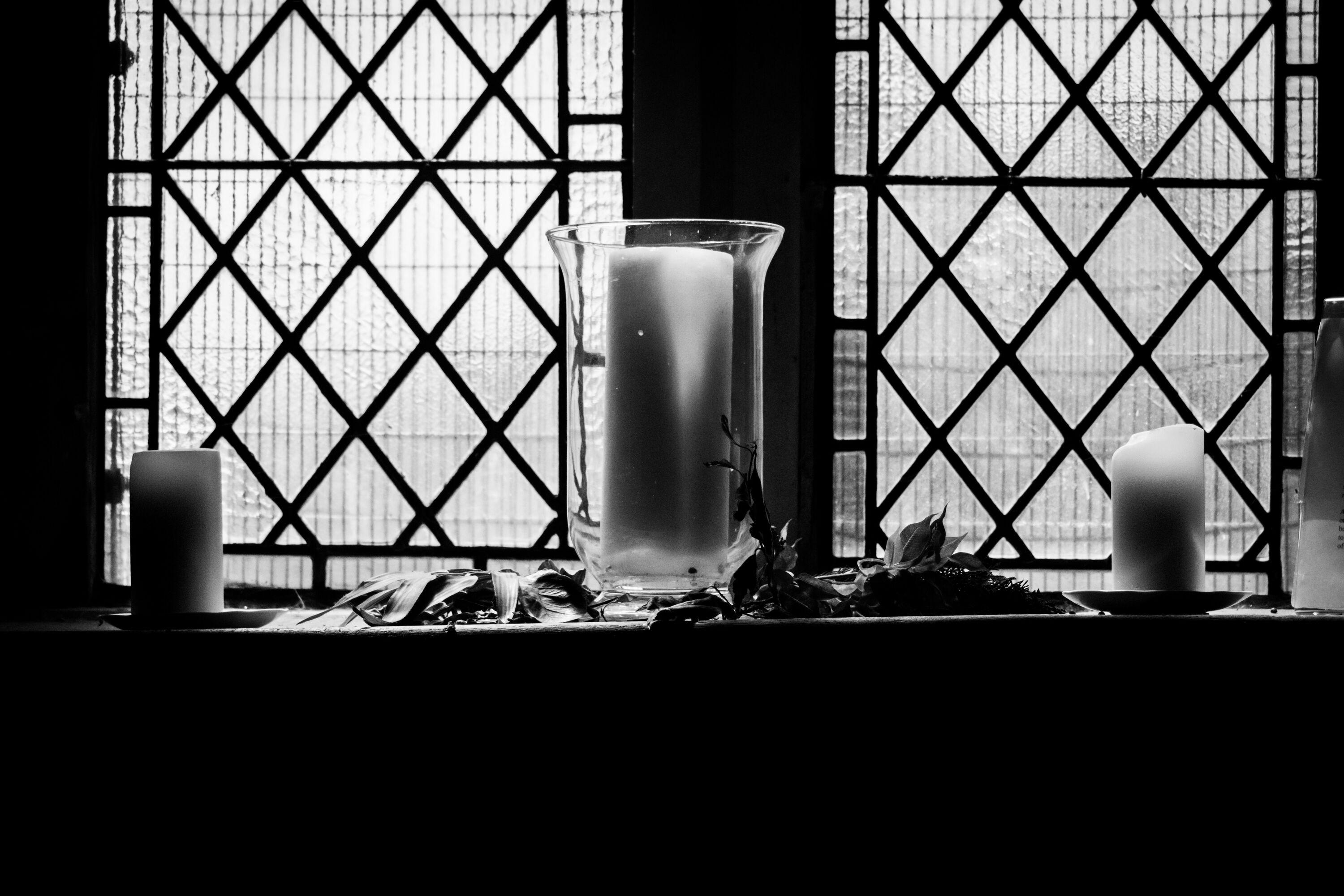Black and white photo of three candles in front of a window inside a church.