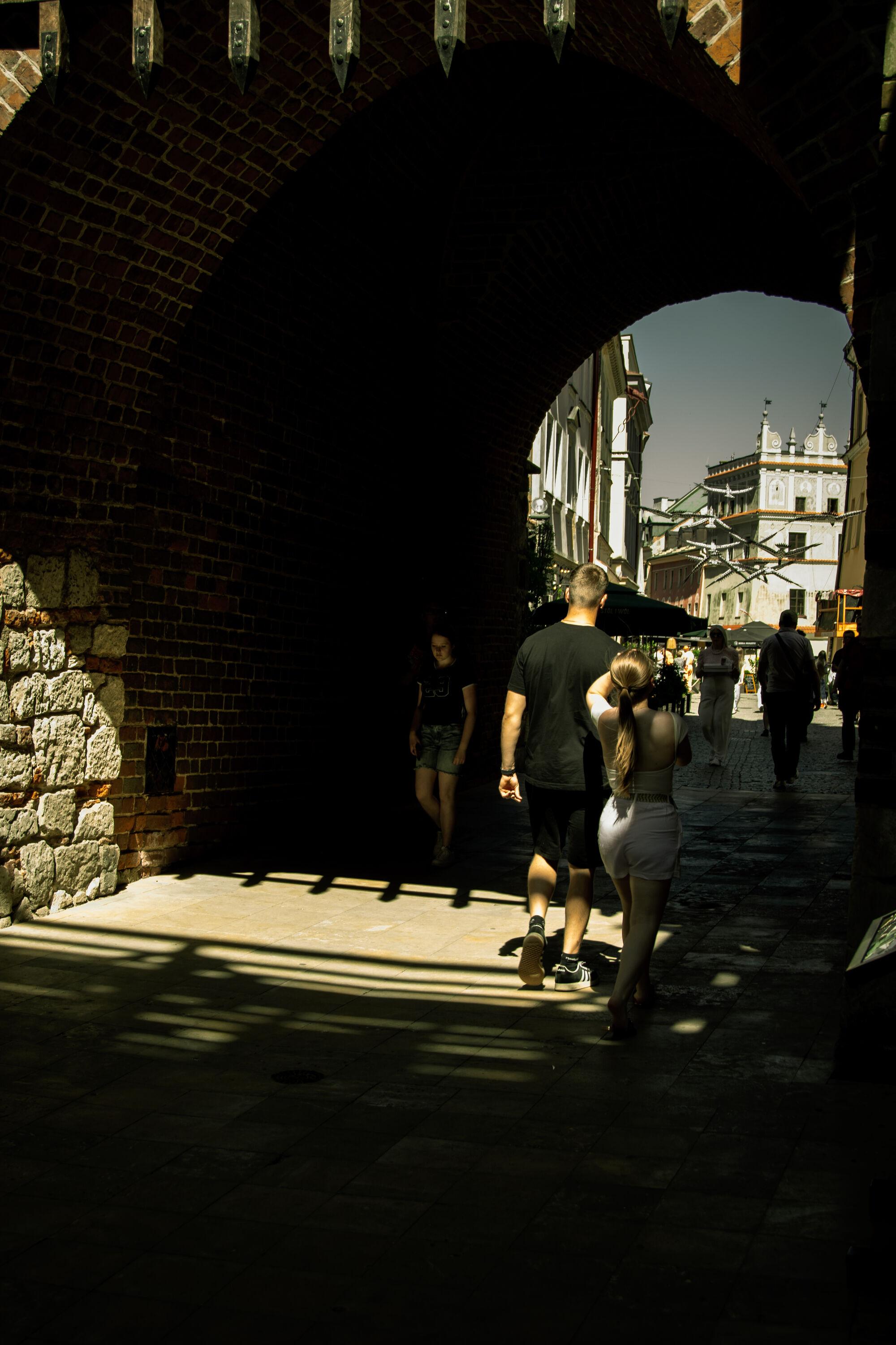 A street scene with pedestrians passing underneath the dark shadows of the old city gate.