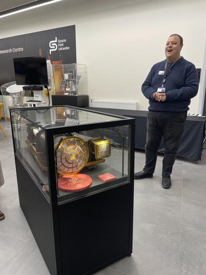 Photo of an enthusiastic man in front of a case with an x-ray telescope, part of a fantastic tour covering the contributions of Leicester and other UK universities to space travel and research 